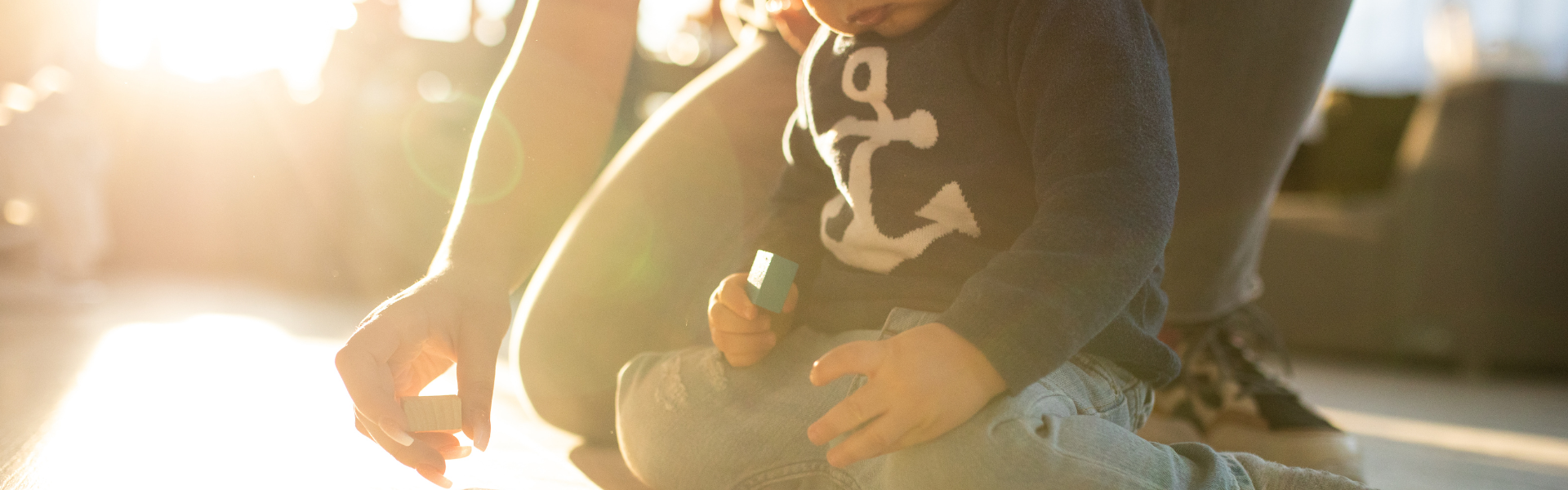 a toddler playing with blocks with parent's arms behind them