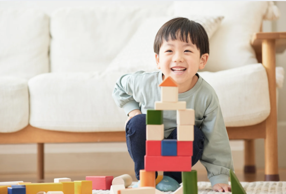 Smiling young child building a colorful block tower on the floor.