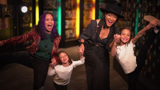 Snooknuk holding hands with two children while dancing indoors